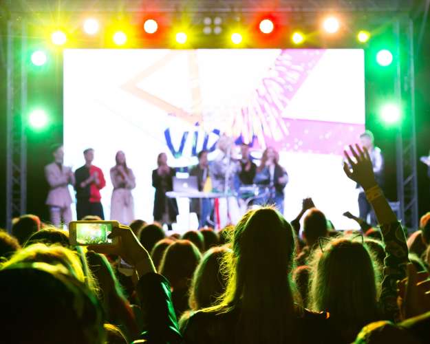 Large crowd of people in neon spotlights at an open-air concert